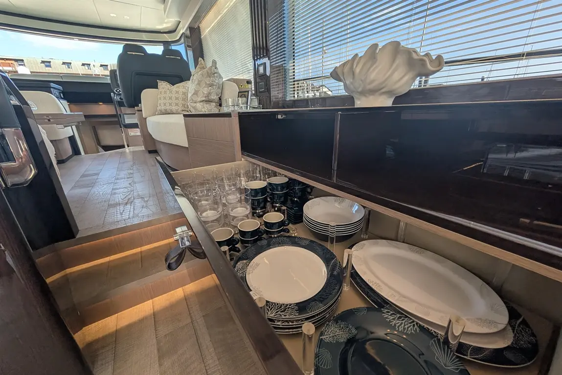 A luxurious boat interior featuring a well-organised cabinet with glassware, china plates, and a decorative shell sculpture.